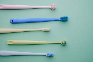 Ağız temizliği için açık yeşil arka planda çapraz dizilmiş beş renkli diş fırçası.