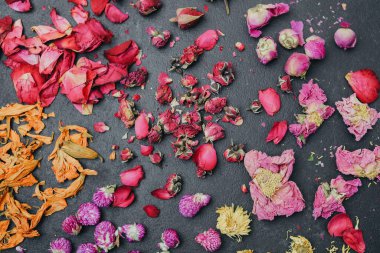 Kurumuş çiçekler ve yapraklar koyu bir yüzeye saçılmış, çeşitli renkler ve dokular doğal bir soyut desen oluşturur..