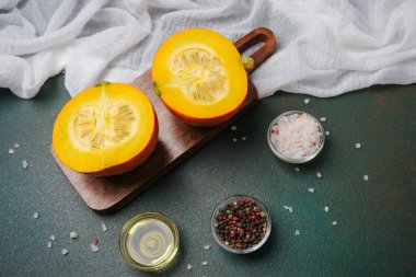 Ahşap tahtada ikiye bölünmüş turuncu balkabağı ve koyu arkaplanda tuz ve karabiber kaseleri.