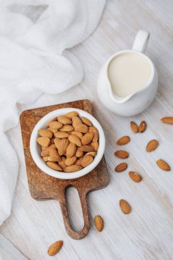 Tahta tahtada sürahi badem sütü ve açık arkaplanda badem.