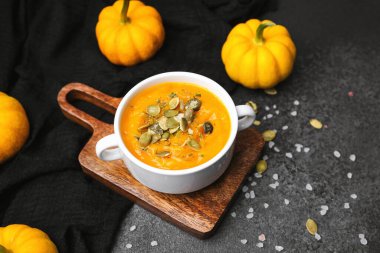 Tahta bir tahtanın üzerinde küçük balkabaklarıyla servis edilen çekirdekli ve otlu balkabağı çorbası..