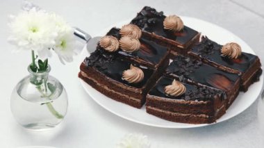 Çürümüş çikolata dilimleri krema kaplı vazoda beyaz çiçekli beyaz bir tabakta servis ediliyor..