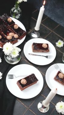 Beyaz tabaklarda servis edilen çikolatalı pasta ve mum yanında beyaz çiçekler.