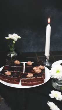 Beyaz çiçekli, siyah çikolatalı pasta dilimleri ve yanan mum.