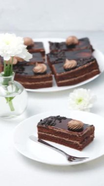 Beyaz çiçekli beyaz tabaklar ve çatallı lezzetli çikolatalı pasta dilimleri.