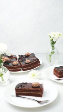 Kremayla süslenmiş çikolatalı pasta ve beyaz tabakta çiçekler.