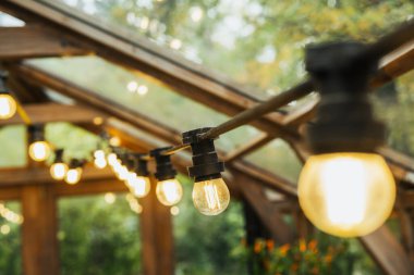 Sicim ışıkları, yeşil ağaçlı, kırsal ahşap bir serayı aydınlatan ılık sarı bir ışık saçıyor.