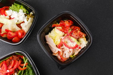 Yemek hazırlama ya da sağlıklı yemek hazırlama konsepti için içinde gurme malzemelerinin bulunduğu siyah kaplarda çeşitli taze salatalar.