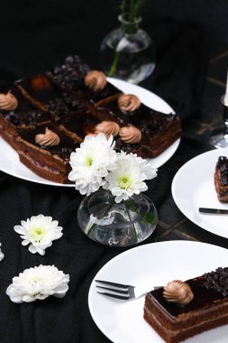 Kremalı tatlı çikolatalı pasta dilimleri ve koyu arkaplanda çiçekler.