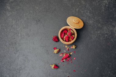 Kurumuş kırmızı gül tomurcukları, koyu dokulu bir yüzeyde, ahşap bir kabın içinde.