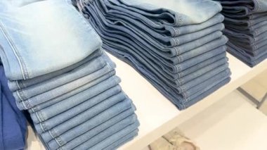 Bir giyim mağazasında beyaz raflarda düzgünce katlanmış mavi kot pantolon.