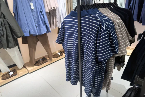 Parlak bir perakende alanındaki askılarda çizgili polo tişörtleri ve günlük erkek kıyafetlerini göster.