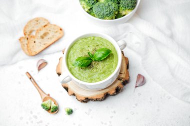 Taze fesleğenli yeşil kremalı brokoli çorbası ve beyaz bir masada kabuklu ekmekle servis edilen sarımsak.