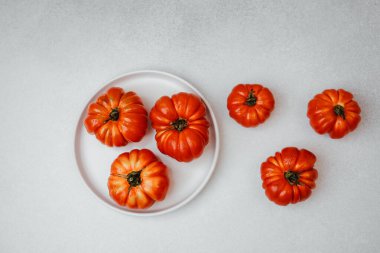Beyaz bir tabakta su damlaları ve açık gri arka planda olgun kırmızı domatesler..
