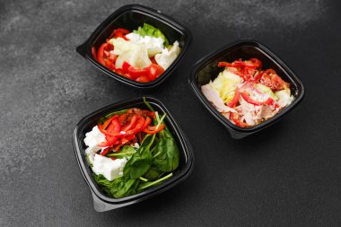 Yemek hazırlama ya da sağlıklı yemek hazırlama konsepti için içinde gurme malzemelerinin bulunduğu siyah kaplarda çeşitli taze salatalar.