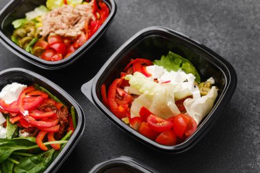 Restoran teslimatı ya da yemek hazırlama konsepti için siyah kaplarda taze sebzelerle karışık salatalar et peyniri ve yeşillikler.