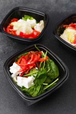 Yemek hazırlama ya da sağlıklı yemek hazırlama konsepti için içinde gurme malzemelerinin bulunduğu siyah kaplarda çeşitli taze salatalar.