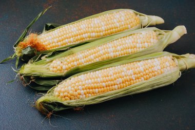 Mevsimlik tarım hasadı ya da sağlıklı yemek malzemesi fotoğrafçılığı için kabuklu üç taze mısır koçanı.