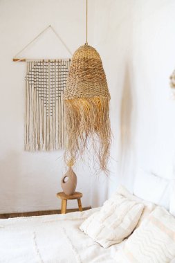 Yatağın üstünde doğal fiber kolye ışığı, örülmüş duvar dekoru ve yastıkları var.