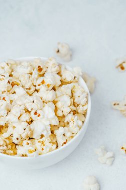 Bir kase kabarık patlamış mısır pürüzsüz, hafif bir yüzeyde, dağınık patlamış mısırla oturuyor..