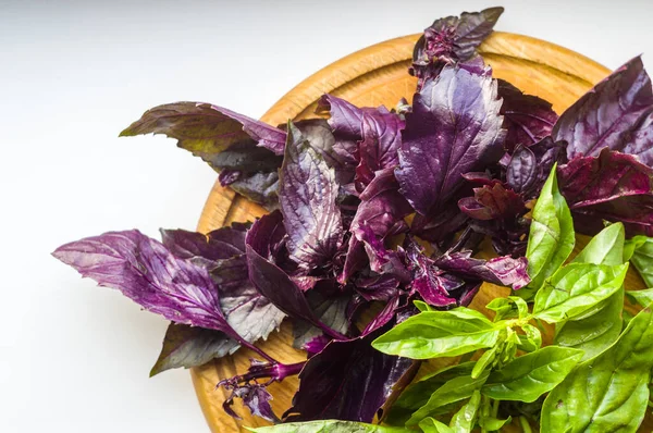 fresh green and purple basil leaves for healthy cooking, herbs and spices on wooden cutting board, closeup