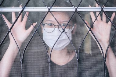 Maske takan genç Asyalı bir kadının portresi ve Covid-19 salgınında kendini evinde karantinaya alması. Karantina, COVID-19 'a maruz kalmış birini diğerlerinden uzak tutmak için kullanılır.