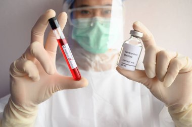 Bilim adamı doktor bir şişe Covid-19 aşısını kan test tüpüyle tutuyor. Aşı, hastalıkları önlemenin ve vücudun bağışıklık sistemini virüse karşı korumanın en etkili yollarından biridir..
