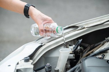 Motorun aşırı ısınmasını azaltmak için insan eliyle arabanın radyatörüne su doldurma görüntüsü. Motorlar aşırı ısınabilir çünkü soğutma sisteminde bir sorun var ve ısı kaçamıyor..
