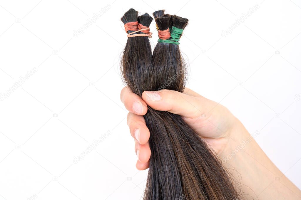 Close up of someone hand holding a ponytail cutting hair for donation. Usable hair can turn your long locks into free or low-cost wigs for people with cancer.
