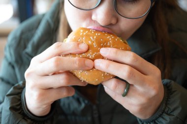 Hamburger yerken genç Asyalı bir kadının görüntüsü. Hamburger, ekmeğin üzerinde pişmiş köfte ya da rulo köfteden oluşan bir sandviçtir..