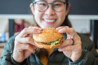 Yemeden önce elinde hamburger tutan Asyalı genç bir kadının portresi. Hamburger, ekmeğin üzerinde pişmiş köfte ya da rulo köfteden oluşan bir sandviçtir..