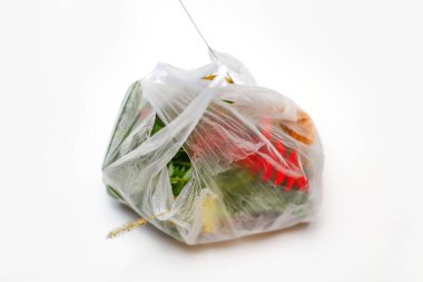 DEFOCUS. Çevreyi koru. Kırmızı ve yeşil bitkiler beyaz arka planda plastik poşette çiçek açarlar. Kuru bir ot sapı öne çıkıyor. Ekolojik sorunlar. Odaklanamıyorum