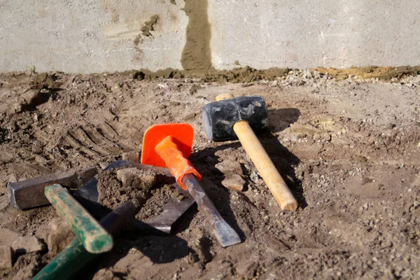 Çekiç, çekiç, çekiç, keski ve süngü yerde yatıyor. Asfalt döşemek için gerekli aletler. Bahçeyi taşla kaplamaya hazırlanıyorum. Arka planda beton levhalar var. Odaklanamıyorum.