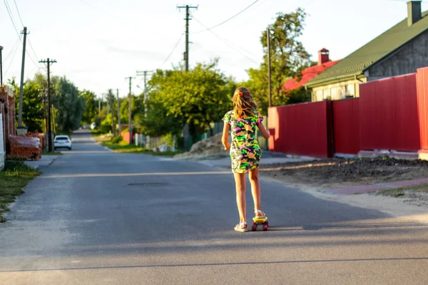Defocus boldog fiatal lány játszik gördeszkán az utcán. Kilátás hátulról. Kaukázusi gyerek pennys deszkán, gördeszkázik. Sport életmód, wellness, aktív hobbi. Nem fókuszált — Stock Fotó