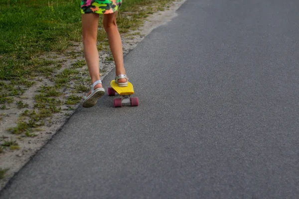Defocus lány játszik sárga gördeszka az utcán és az út mellett. Kaukázusi gyerek pennys deszkán, gördeszkázik. Gyerekkori koncepció. Veszélyes út. Gyors és gyors játék. Nem fókuszált — Stock Fotó