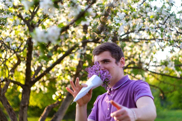 Portrait déconcentré d'un bel homme caucasien avec des fleurs de cône dans un jardin lilas Jeune homme brune drôle et joyeux sentant des fleurs fraîches et regardant la caméra sur fond flou Hors foyer — Photo
