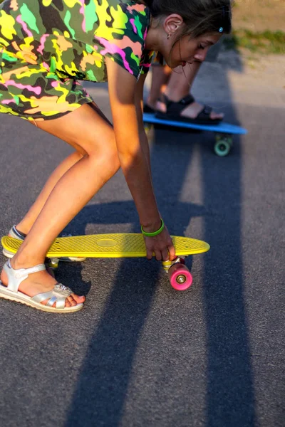 Desenfoque niña feliz y niño jugando en el monopatín en la calle. Niños caucásicos montando penny board, practicando skate. Concepto de amistad. Día soleado. Sombras profundas. Fuera de foco —  Fotos de Stock