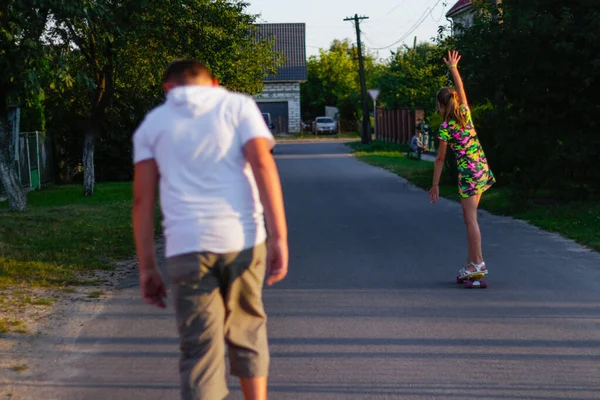 Defocus heureux jeune fille et garçon jouant sur le skateboard dans la rue. Elle a levé les bras. Des enfants caucasiens chevauchant un penny board, pratiquant le skateboard. Concept d'amitié. Hors foyer — Photo