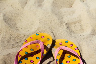 Kirli, parlak sarı ve pembe terlikler üzerinde pembe ve mavi kalpler olan terlikler. Yaz dönemi. Sıcaklık, rahatlama ve iyileşme kavramı, tatil. Odaklanamıyorum.