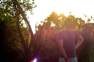 Gün batımında kendine güvenen genç bir adamın silueti. Bulanık yaz ağaçları. Kafkasyalı bir adamın silueti. Parlak güneş ışığı ve gökyüzü. Odaklanamıyorum.