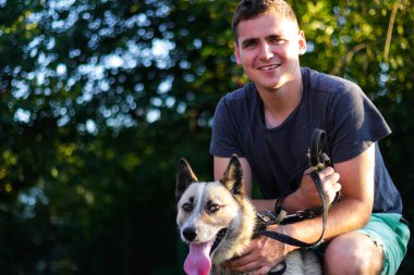 Defocus yakın plan beyaz adam gülümsüyor ve köpekle oturuyor. Yazın Sibirya laika husky açık hava yakınında çömelmiş bir adamın portresi. Arkadaşlık ve sevgi. Bokeh. Odaklanamıyorum.