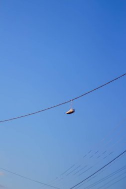 Elektrik tellerinden sarkan Defocus spor ayakkabıları mavi gökyüzü arka planına karşı. Kentsel kültür kavramı, yasaklı maddelerin satışı, getto. Yükseklik. Odaklanamıyorum