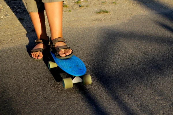 Desenfoque pequeño chico urbano de pie en un monopatín de penique azul. Un niño en el parque. Estilo ciudad. Niños urbanos. Sombras modernas de moda de fondo. Camino de asfalto, carretera. Fuera de foco —  Fotos de Stock