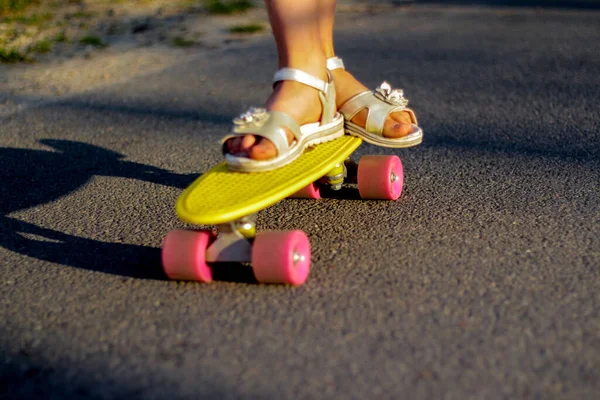 Defocus skater moving along asphalt road on a yellow skateboard wearing white sandals. Some of the legs are on a skateboard close up. Young sport activity. Fun summer. Penny board. Out of focus.