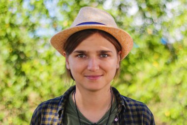 Yakından bakınca, gülümseyen esmer, şapkalı, beyaz bir kadın. Yaz, bulanık yeşil doğa bokeh arka plan. Yakışıklı bir genç kadının portresi. Odaklanamıyorum.