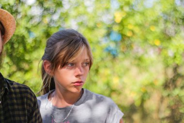 Yakın plan, ergen, ciddi, sarışın, beyaz bir kız. Yaz, bulanık yeşil doğa bokeh arka plan. Kafası karışmış güzel bir kızın portresi. Odaklanamıyorum.