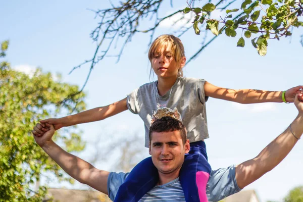 Defocused brother riding sister on back. Portrait of happy girl on man shoulders, piggyback. Girl fly, raise hands. Family playing outdoor. Blue green nature background. Out of focus — Stock Photo, Image