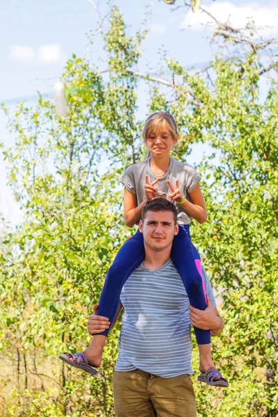 Defocused brother giving sister ride on back. Portrait of happy girl on man shoulders, piggyback. Family playing outside. Summer holidays smiling people concept. Funny horns. Vertical. Out of focus