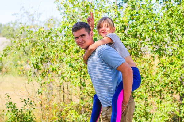 Defocused brother giving sister ride on back. Portrait of happy girl with funny horns on man shoulders, piggyback. Family playing outdoor. Summer holidays vacation happy people concept. Out of focus — Stock Photo, Image