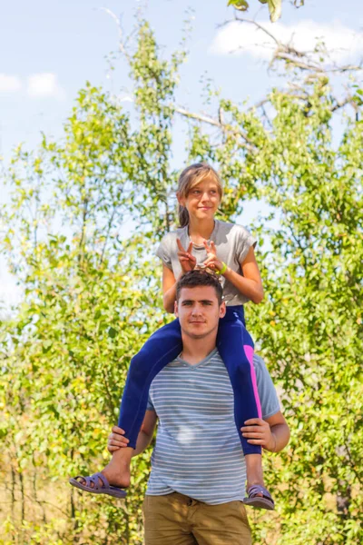 Defocused brother giving sister ride on back. Portrait of happy girl on man shoulders, piggyback. Family playing outdoor. Summer holidays smiling people concept. Funny horns. Vertical. Out of focus — Stock Photo, Image